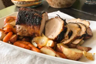 Pork Loin Roast with Veggies - USDA Serving plate with a partially sliced pork loin roast along side cook carrots and potatoes.