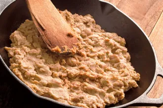 Refried Beans - USDA Cast iron pan containing refried beans. An old wooden spoon rests on top of the beans.