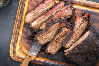 Slow-Cook Barbecue - USDA Overhead view of a tray of several slices of slow-cook barbecue. A knife sits under one slice.