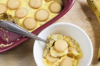Overhead view of a bowl of southern banana pudding with a spoon next to a pan of southern banana pudding with a serving removed.