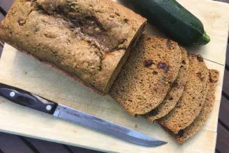 Zucchini Bread - USDA Overhead view of a partially sliced loaf of zucchini bread resting on a cutting board. A knife and whole zucchini rest on either side of the bread.