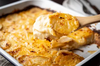 Au Gratin Potatoes - USDA Baking dish of au gratin potatoes with a wooden spoon showing a closer view of the cooked ingredients.