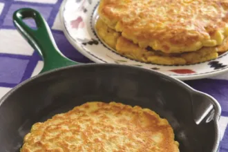 Cooking pan with a cornmeal pancake, next to a plate with two pancakes.